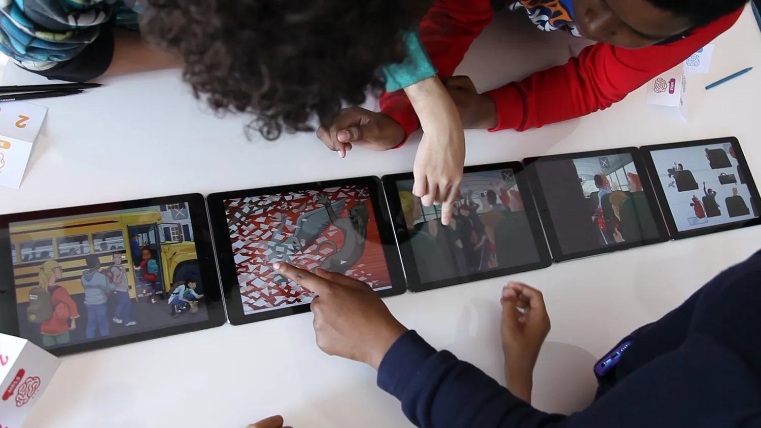Students leaning over a row of tablets on a classroom table, working through Perception Academy together