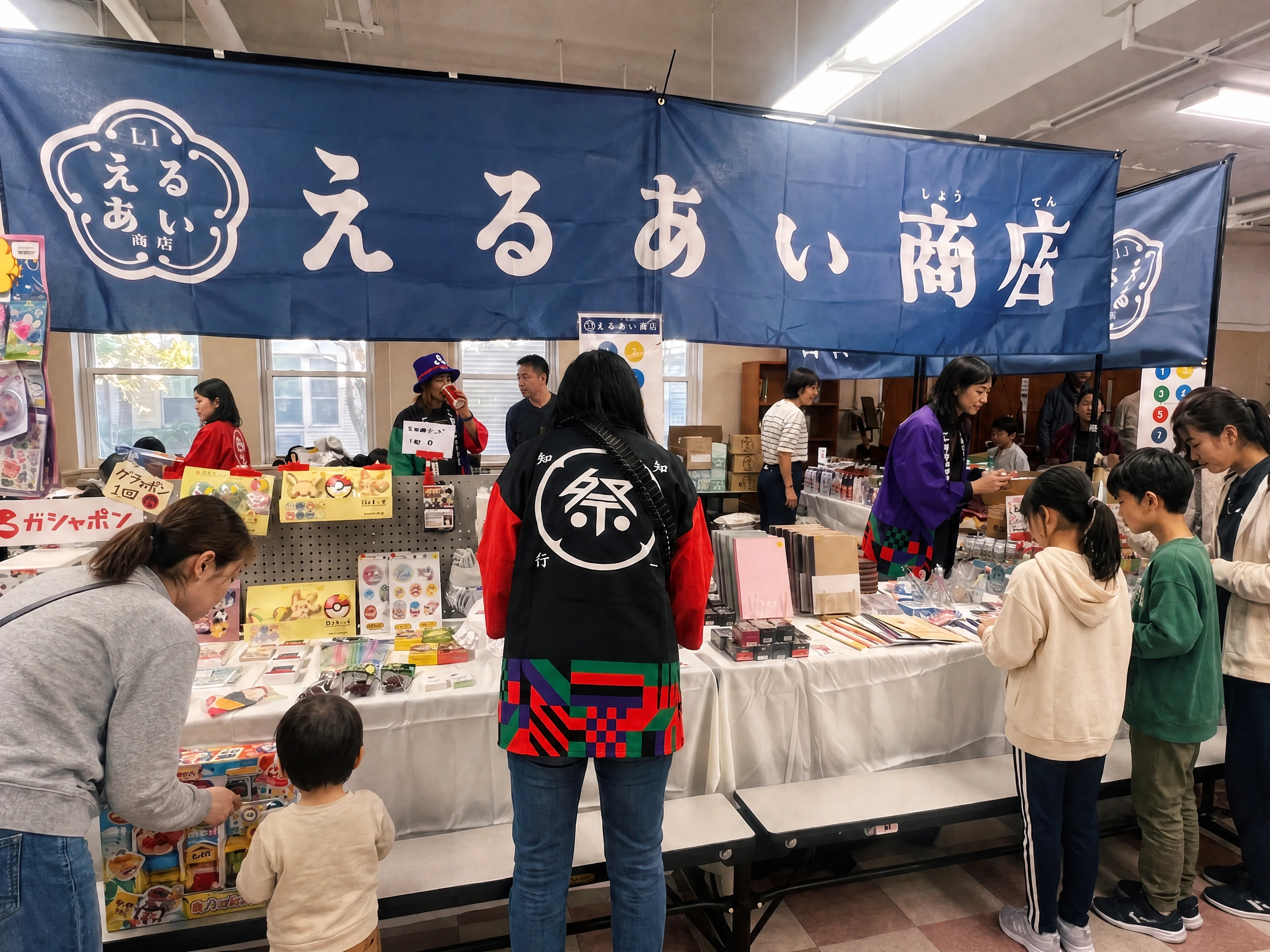 Children and parents browsing merchandise at えるあい商店 under its original navy noren, with adult volunteers in branded happi