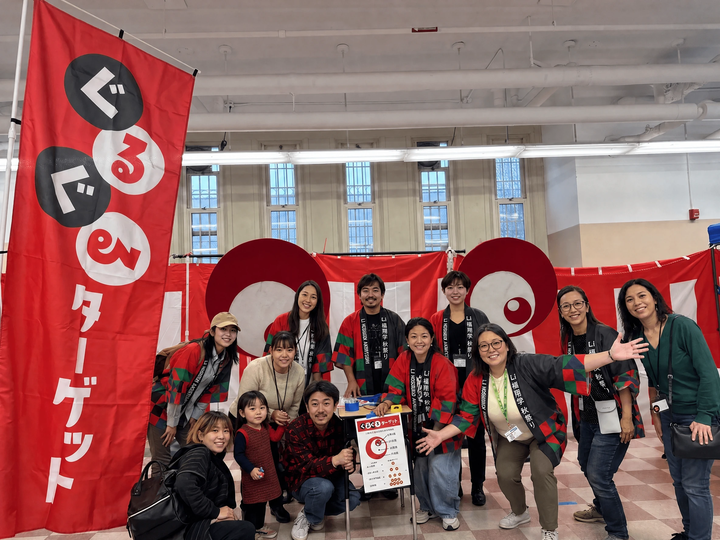 Volunteers and families posing in front of the two eye-shaped targets, with the red Guruguru Target nobori on the left