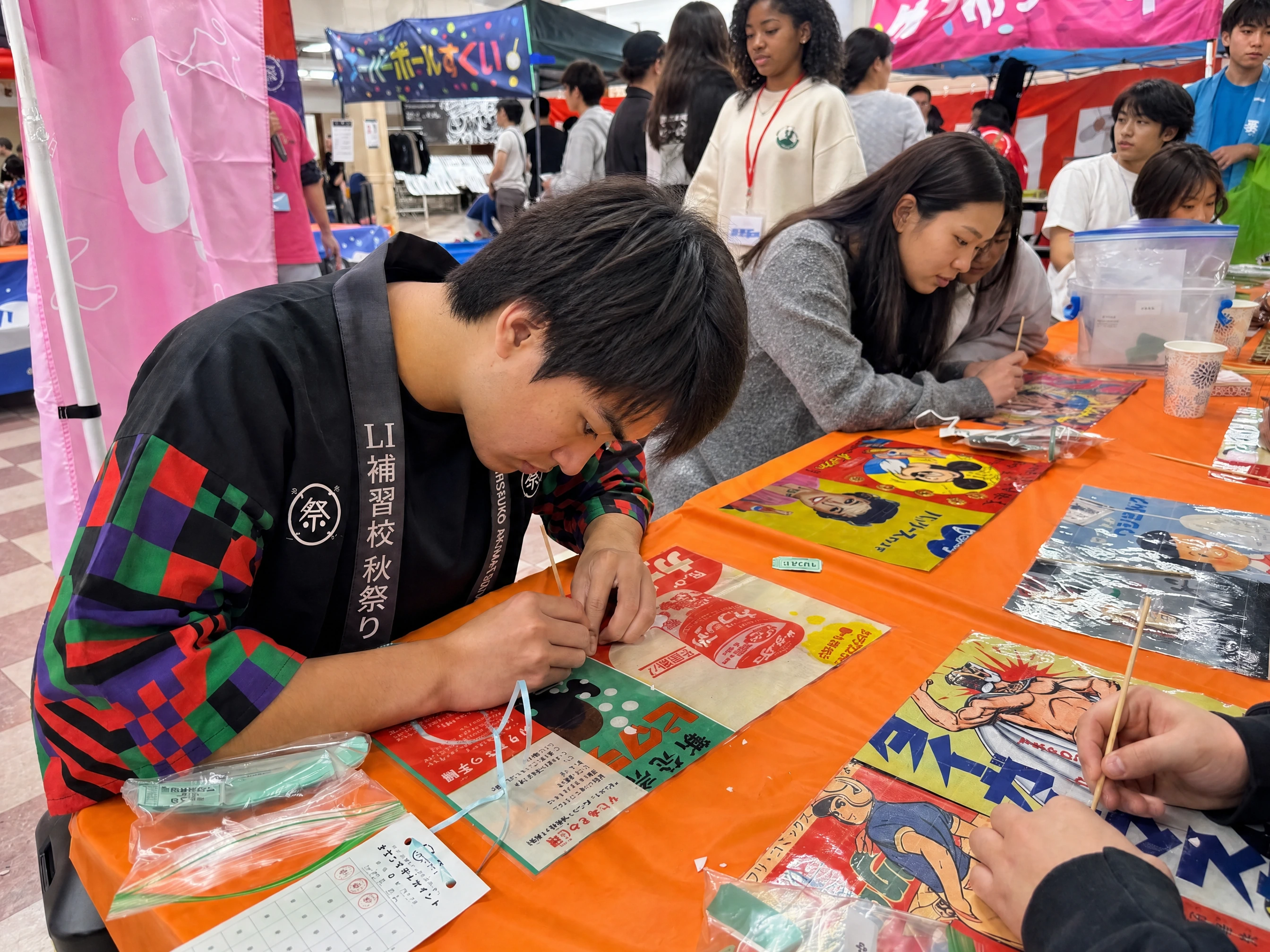 Players bent over the katanuki table, carving tablets with needles on a cloth of retro Showa posters