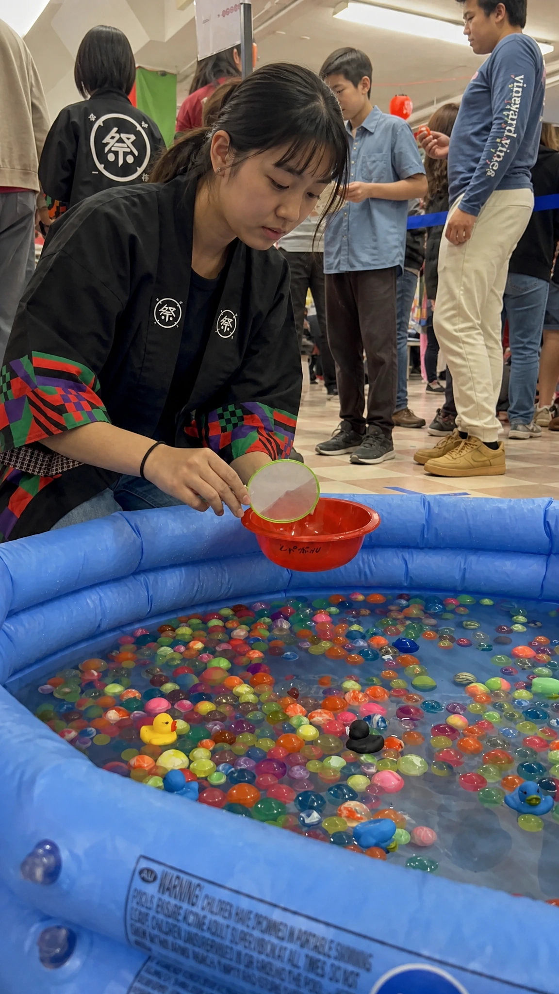 A child lifting a bowl over a pool full of colourful super balls