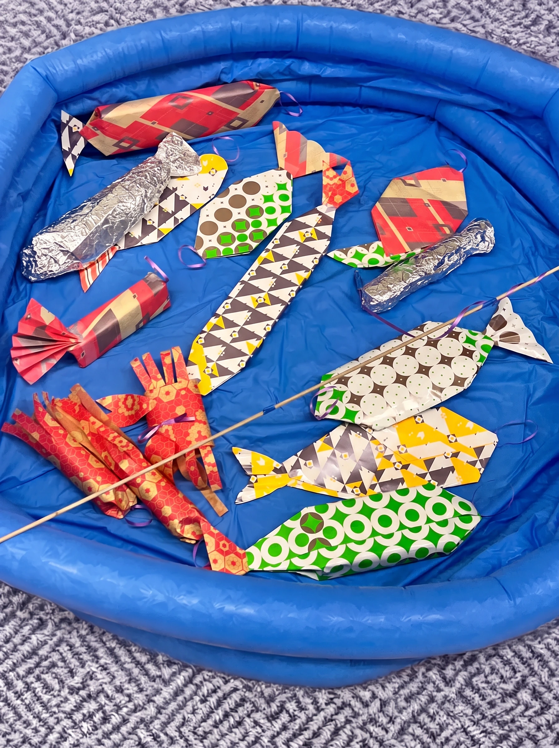 Close-up of the paper and foil fish, each with a coloured loop, lying in a blue pool