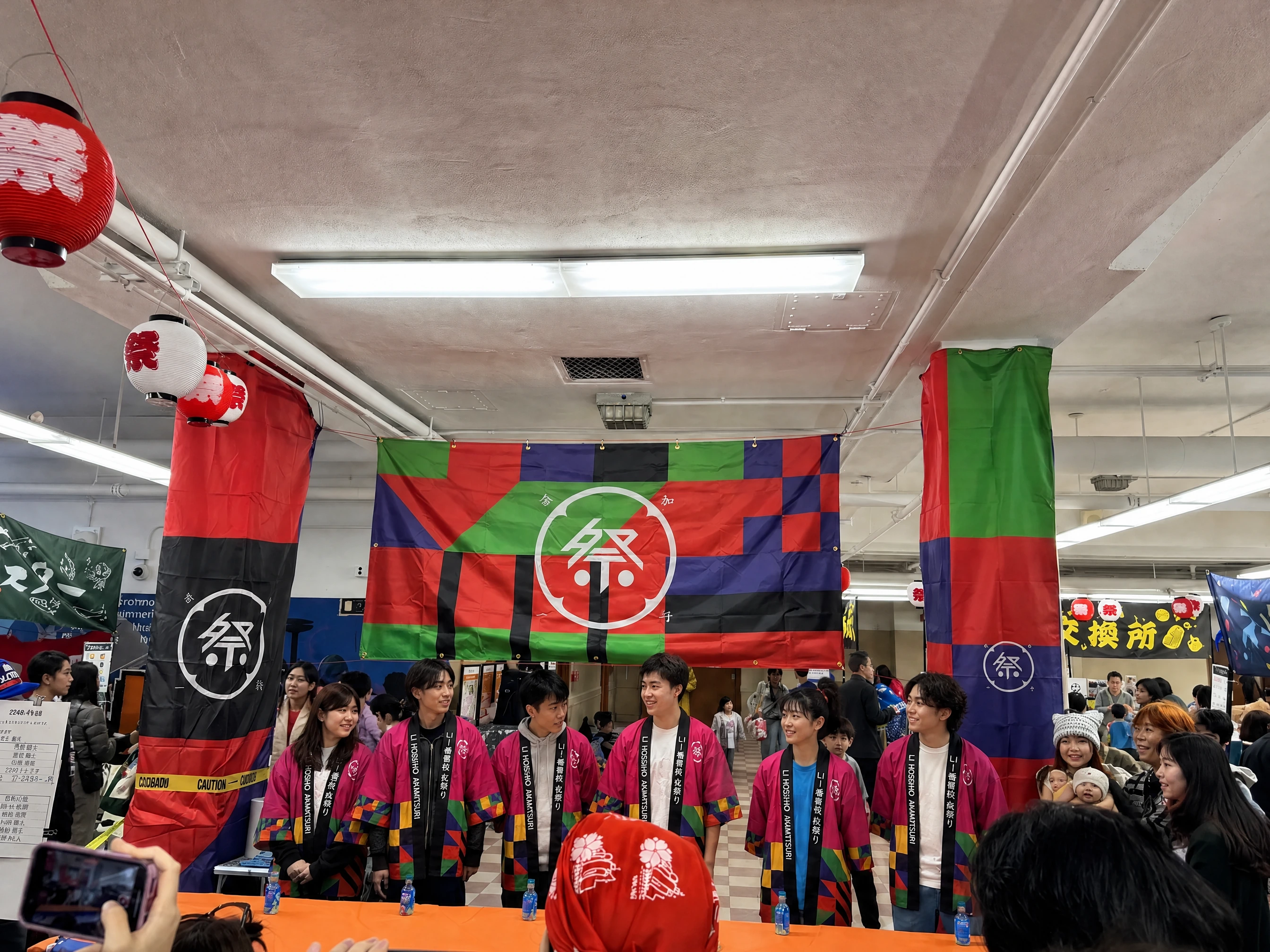 The built entrance on the day: the patterned banner with the mark hung between two patterned pillars, paper lanterns overhead and a crowd below